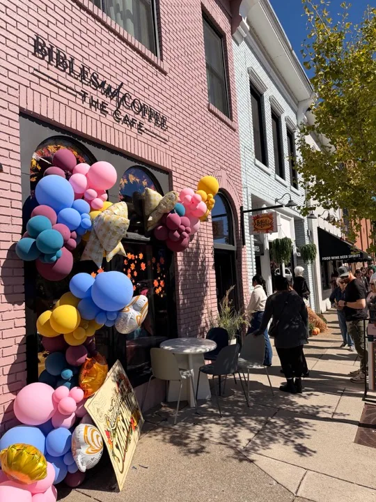 Guests outside the pink Bibles and Coffee storefront decorated with colorful balloons and autumn leaves for Gilmore Girls Weekend